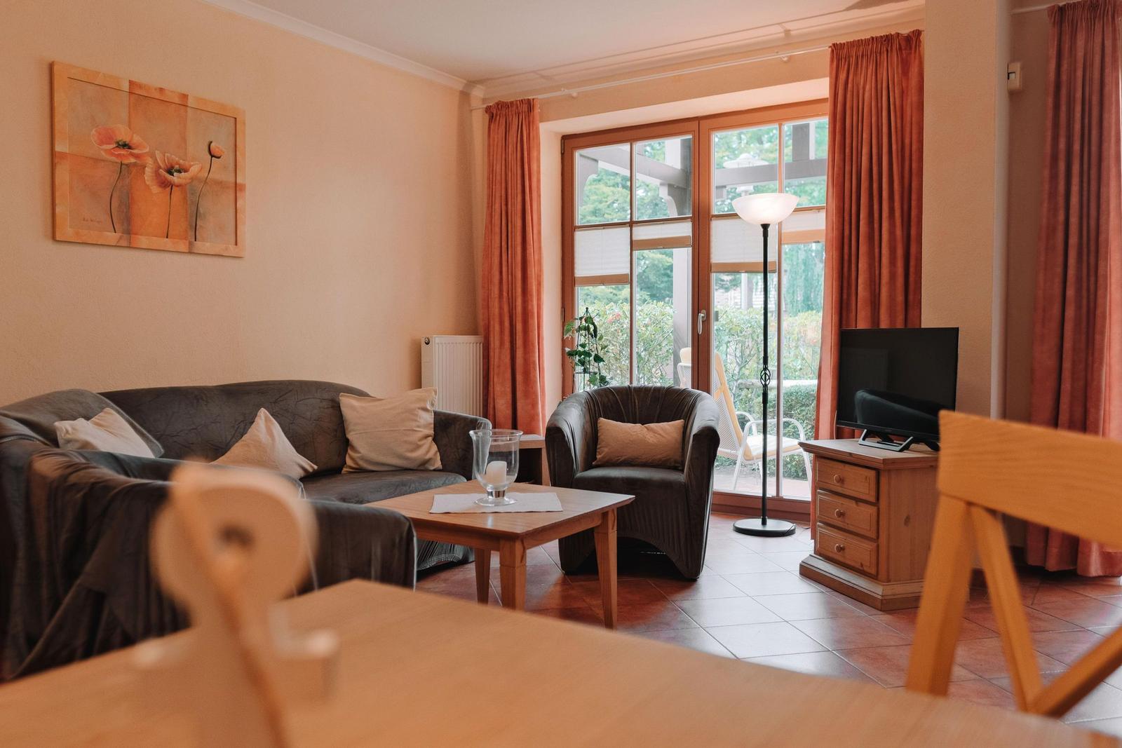 Wohnzimmer mit Sofa, Sessel, Fernseher und Terrassentür.