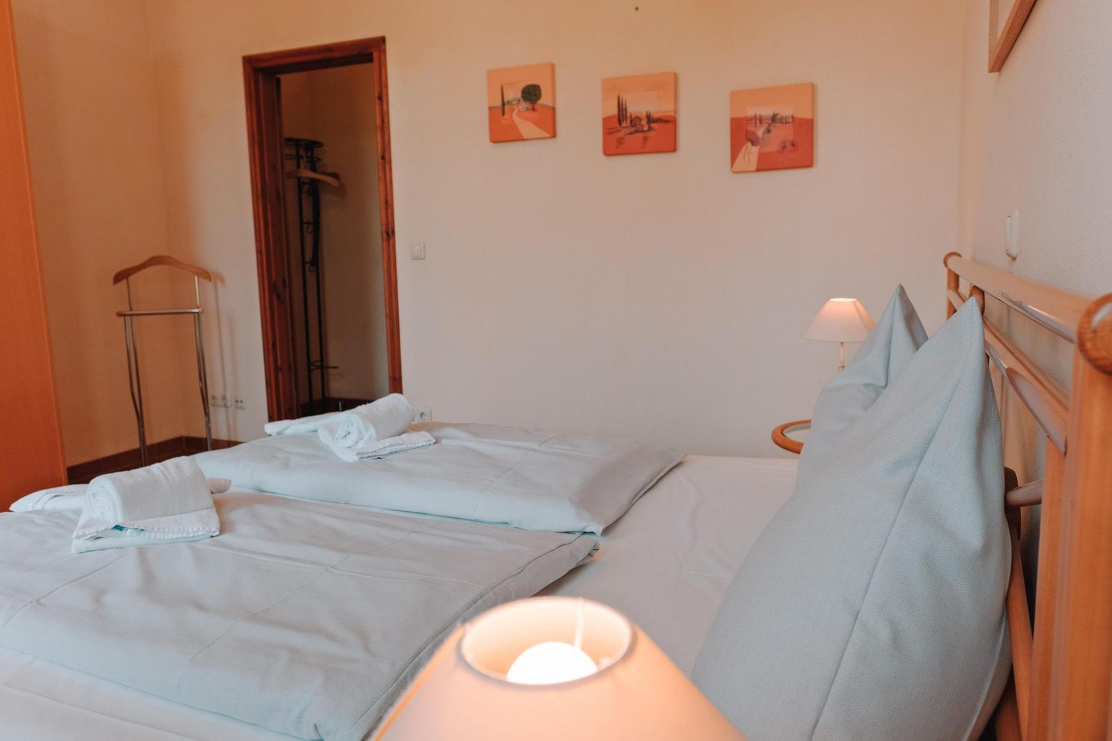 Schlafzimmer mit Bett, Kissen, Lampen und Wandbildern.