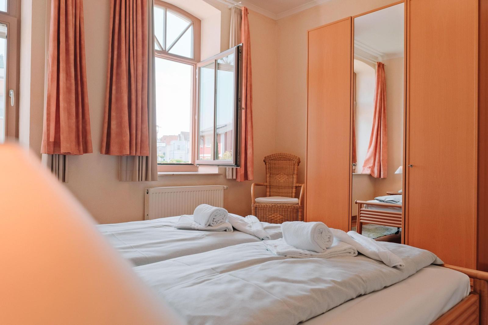 Zimmer mit Doppelbett, Fenster, Gardinen und Spiegelschrank.