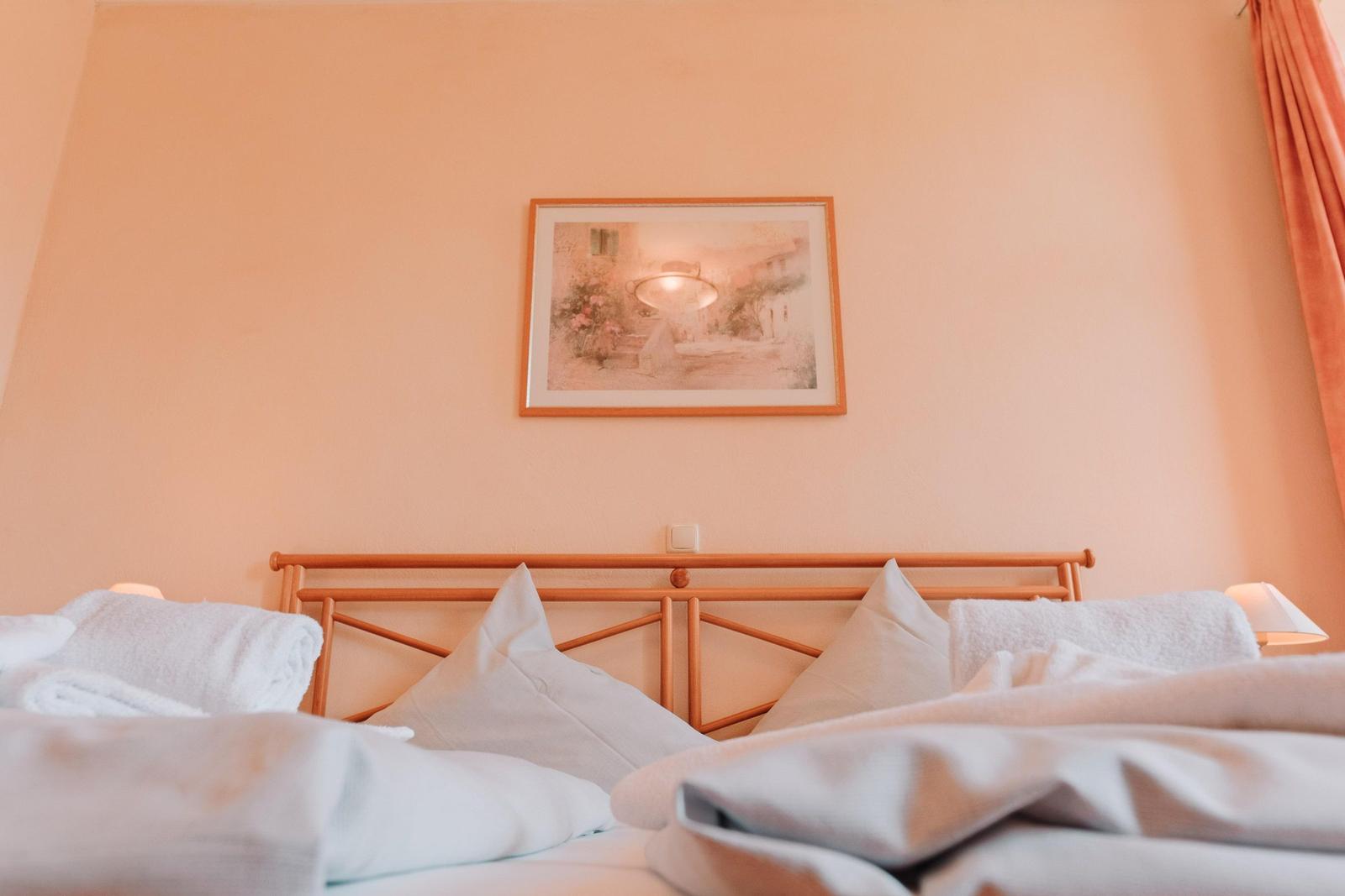 Ein Bett mit weißen Kissen und Decken, Wandbild und Vorhang.