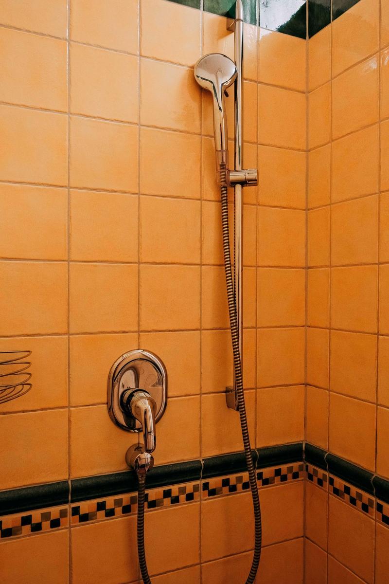 Dusche mit Handbrause und orangefarbenen Fliesen