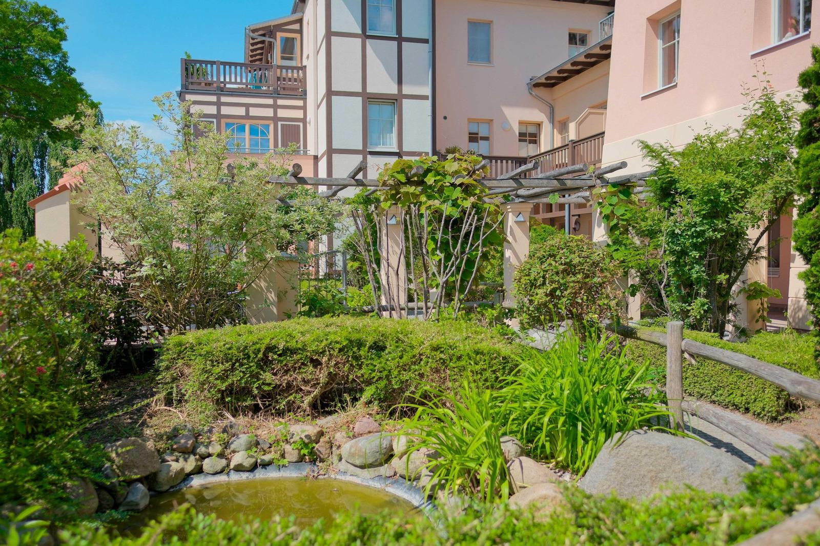 Garten mit Teich, Sträuchern und Pergola vor mehrstöckigem Haus