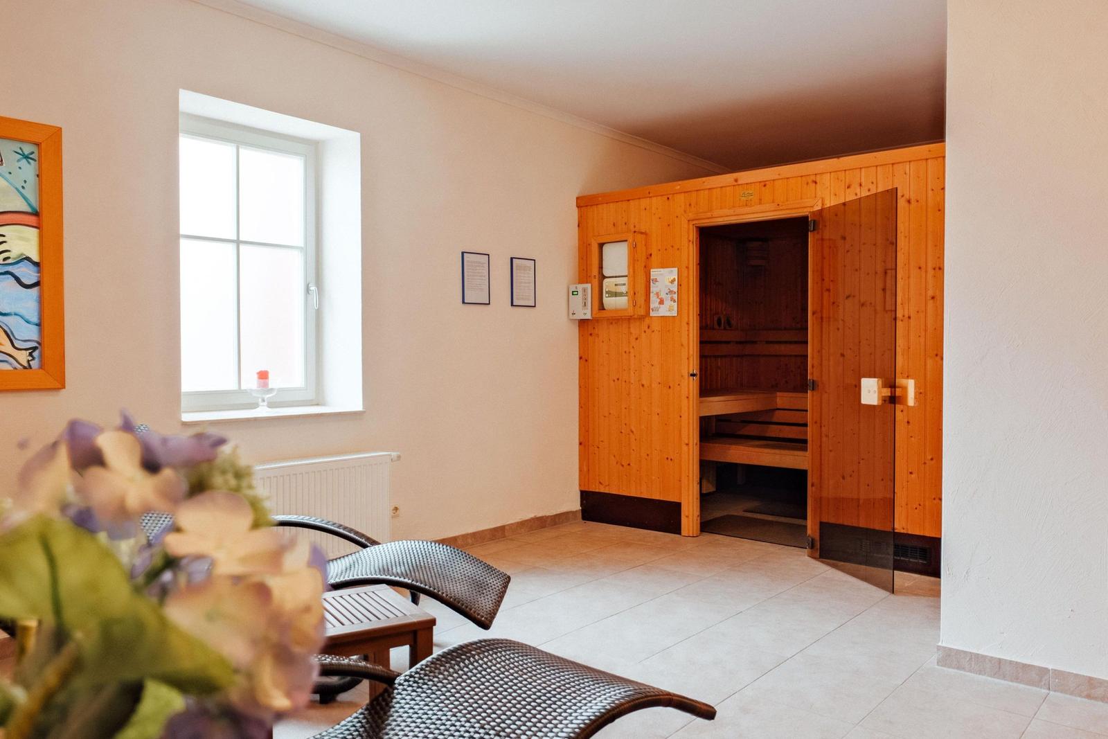 Sauna mit Holzverkleidung und Sitzbänken. Fenster, Wandbilder und Sitzgelegenheiten im Vordergrund.