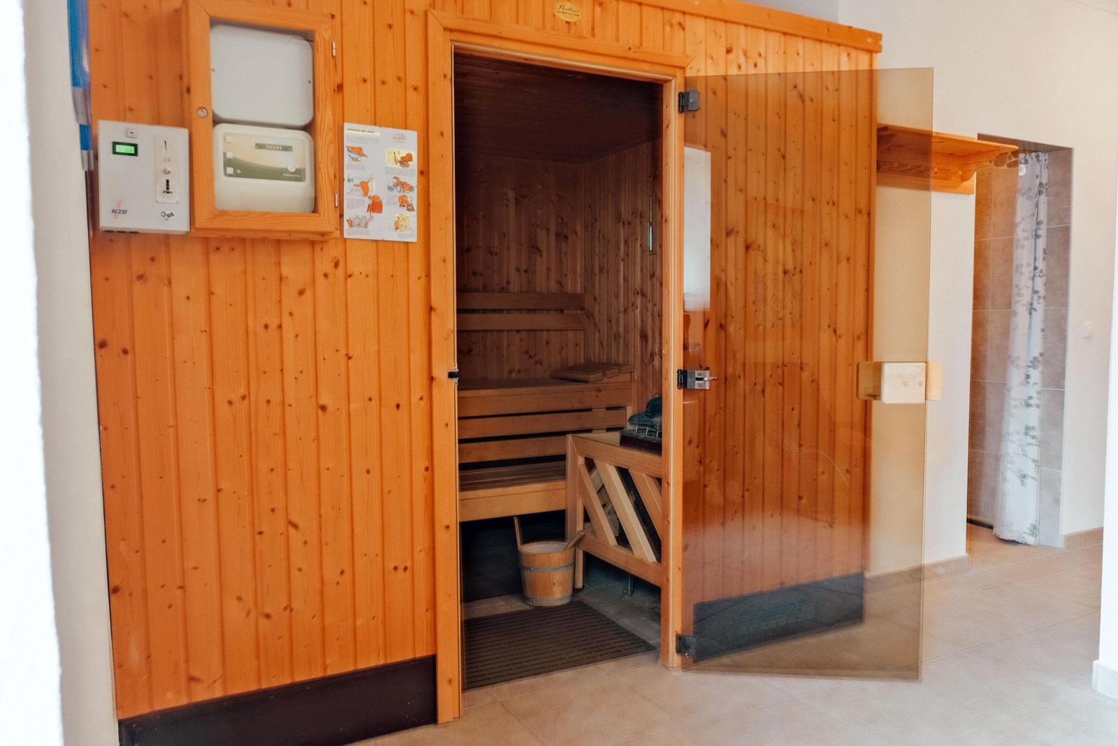 Sauna mit Holzbank und Eingangstür. An der Wand sind Steuerungseinheit und Anleitung angebracht.