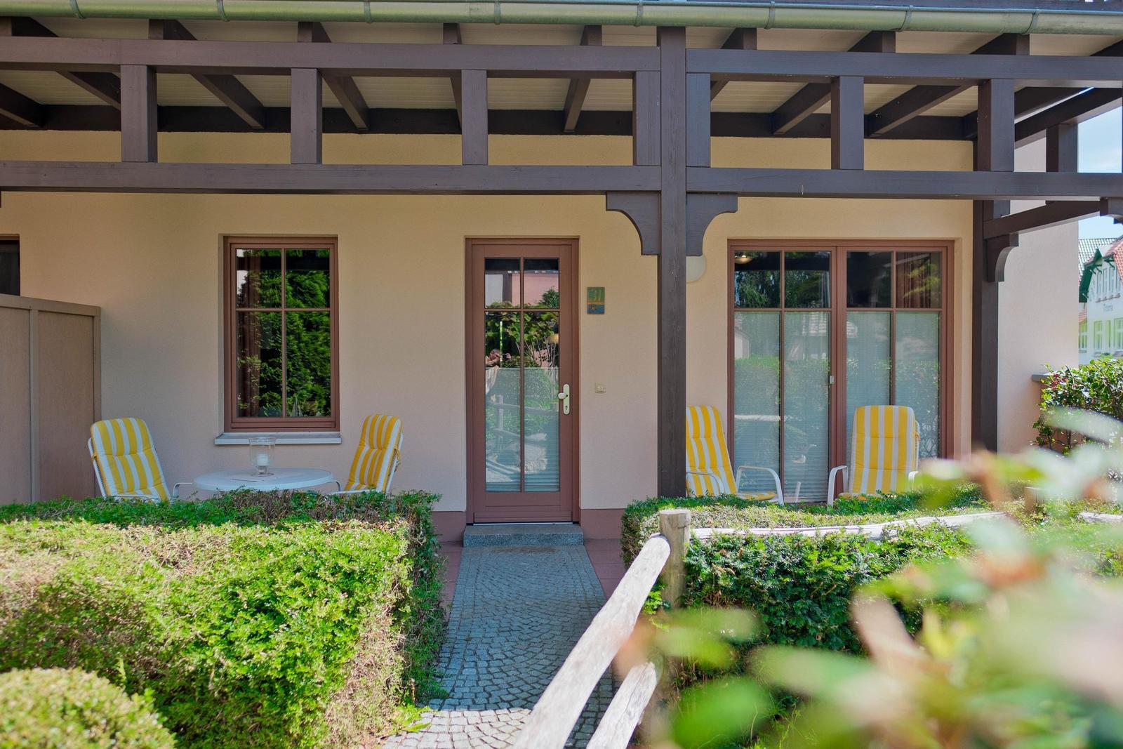 Haus mit Terrasse, gelben Stühlen und gepflastertem Weg.
