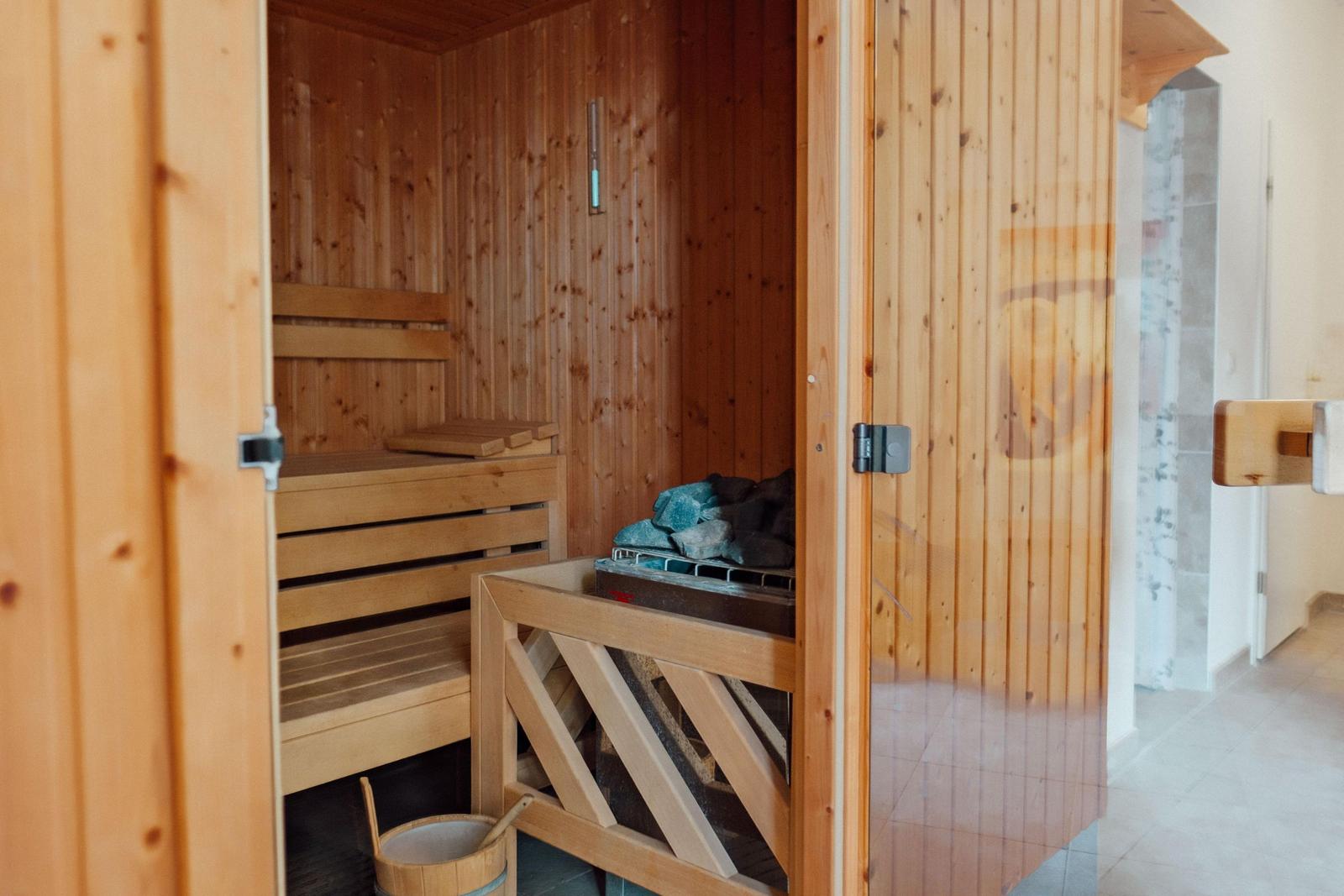 Holzsauna mit Bänken und Steinen. Tür offen, Blick ins Innere.