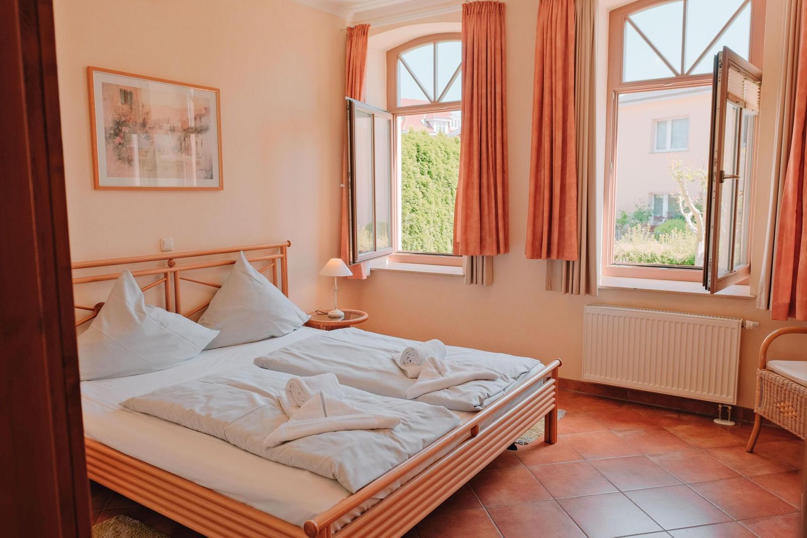 Schlafzimmer mit Doppelbett, zwei Fenstern und Terrakottaboden.