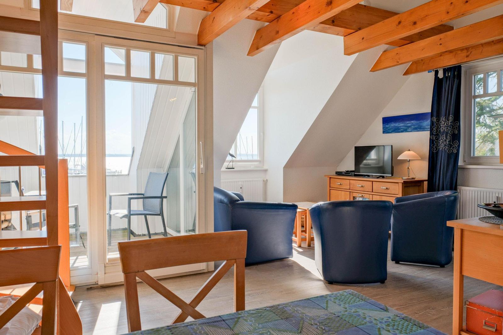 Wohnraum mit blauen Sesseln, Holzbalken und Blick auf den Hafen.