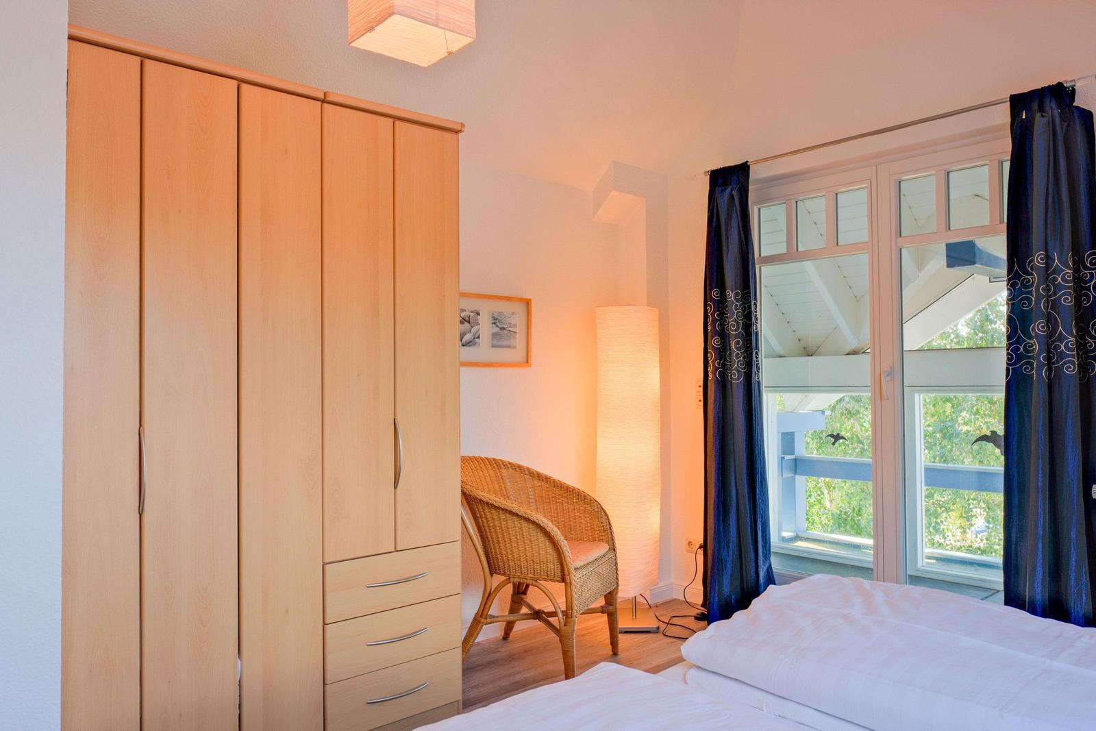 Schlafzimmer mit Doppelbett, Kleiderschrank und Blick auf Balkon.