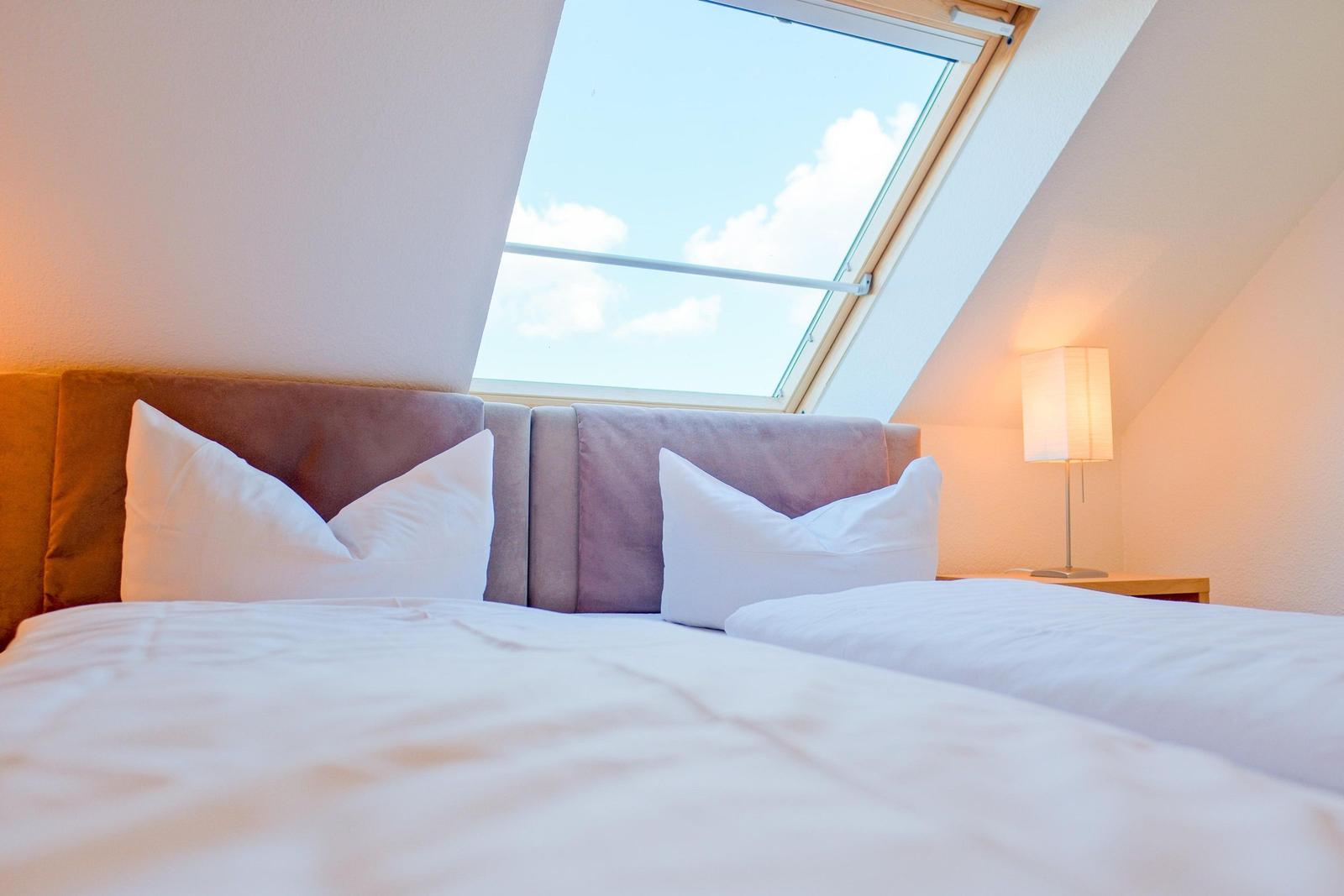 Doppelbett mit weißen Kissen unter Dachfenster mit Blick auf Himmel