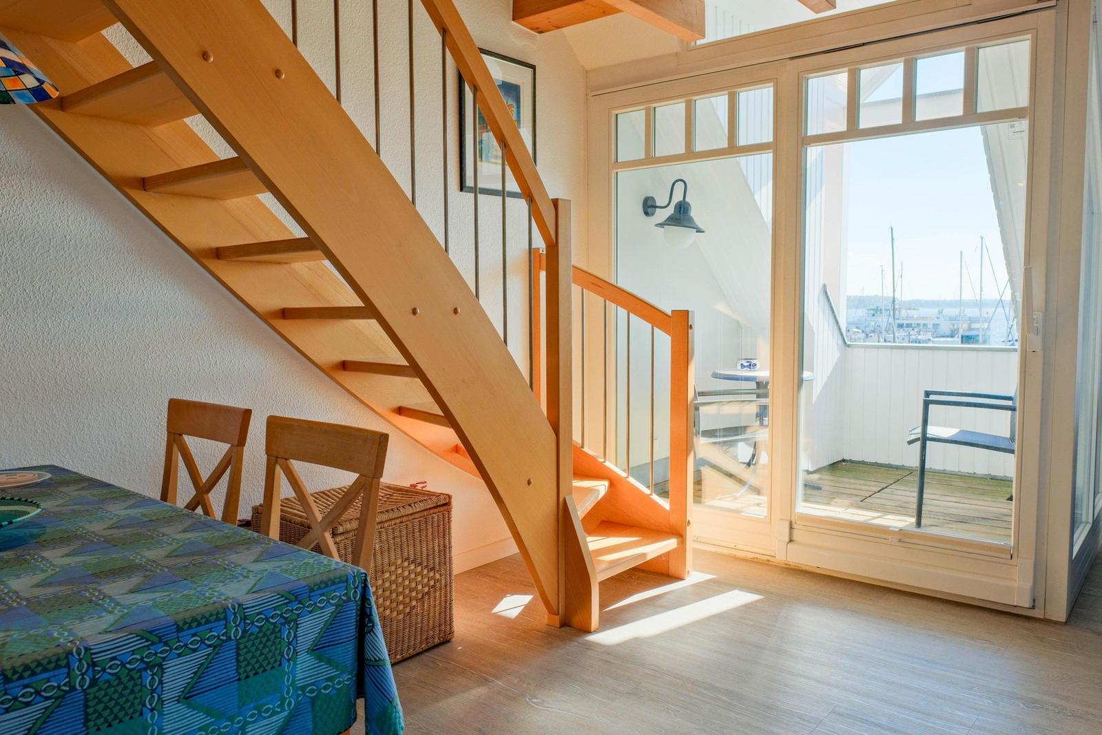 Holztreppe führt zur Terrasse mit Blick auf Hafen. Tisch mit Stühlen und Korb unter der Treppe.