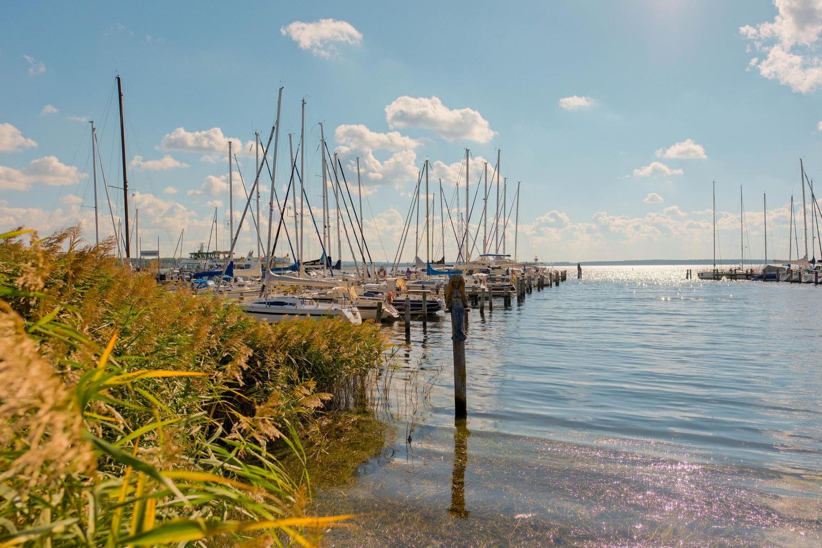 Hafen mit Segelbooten und ruhigem Wasser unter blauem Himmel.