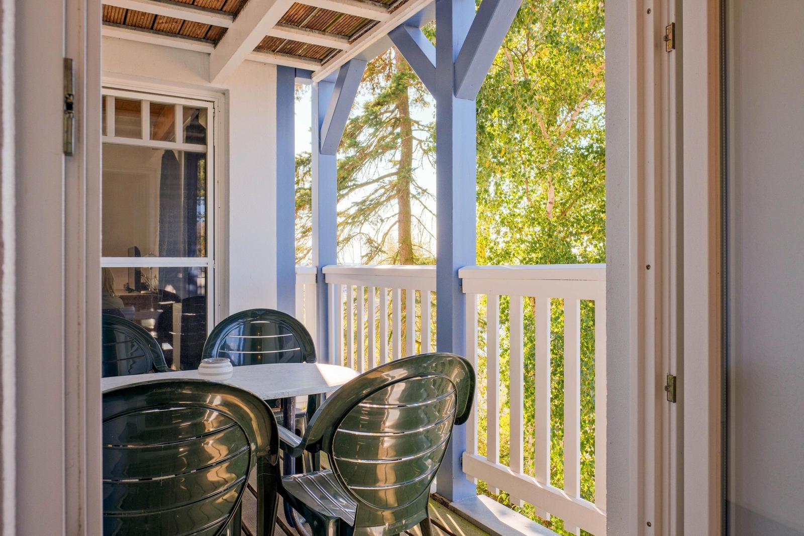 Terrasse mit Tisch und Stühlen, Blick auf Bäume und blauen Pfosten.