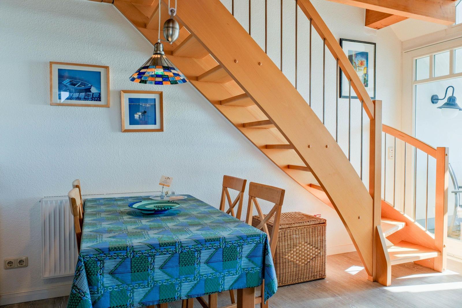 Esszimmer mit Holztreppe und Tisch mit blauem Tischtuch.