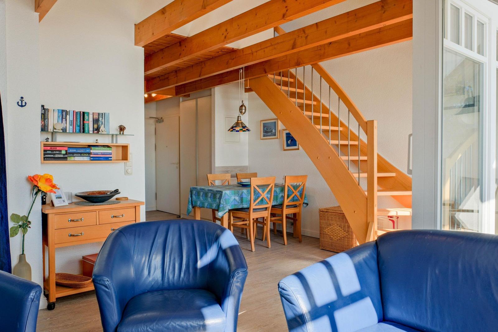 Wohn- und Essbereich mit Holzstufen, blauen Sesseln und Tisch mit Stühlen.