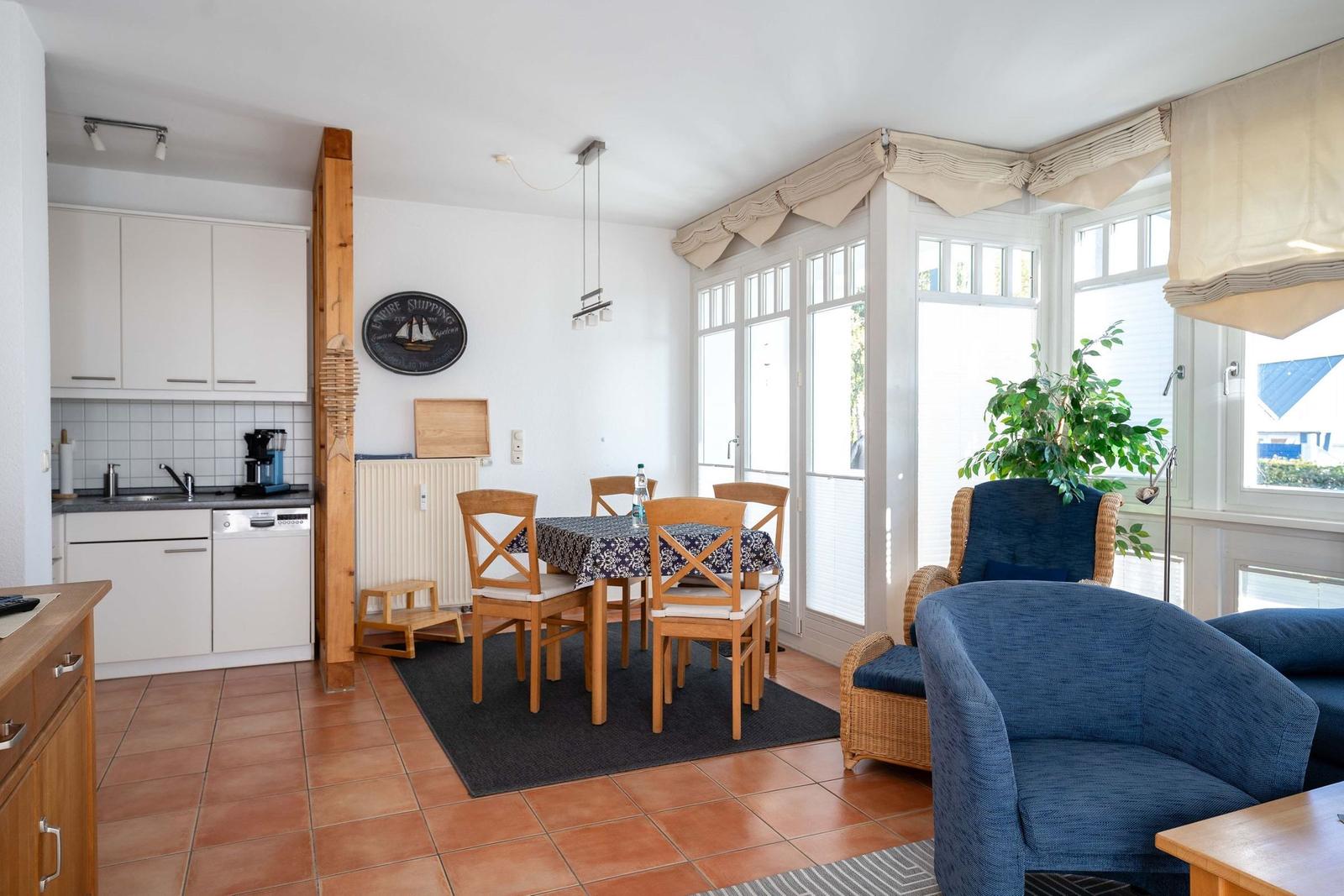 Küche, Essbereich und Wohnbereich mit blauen Sesseln und Holzmöbeln.