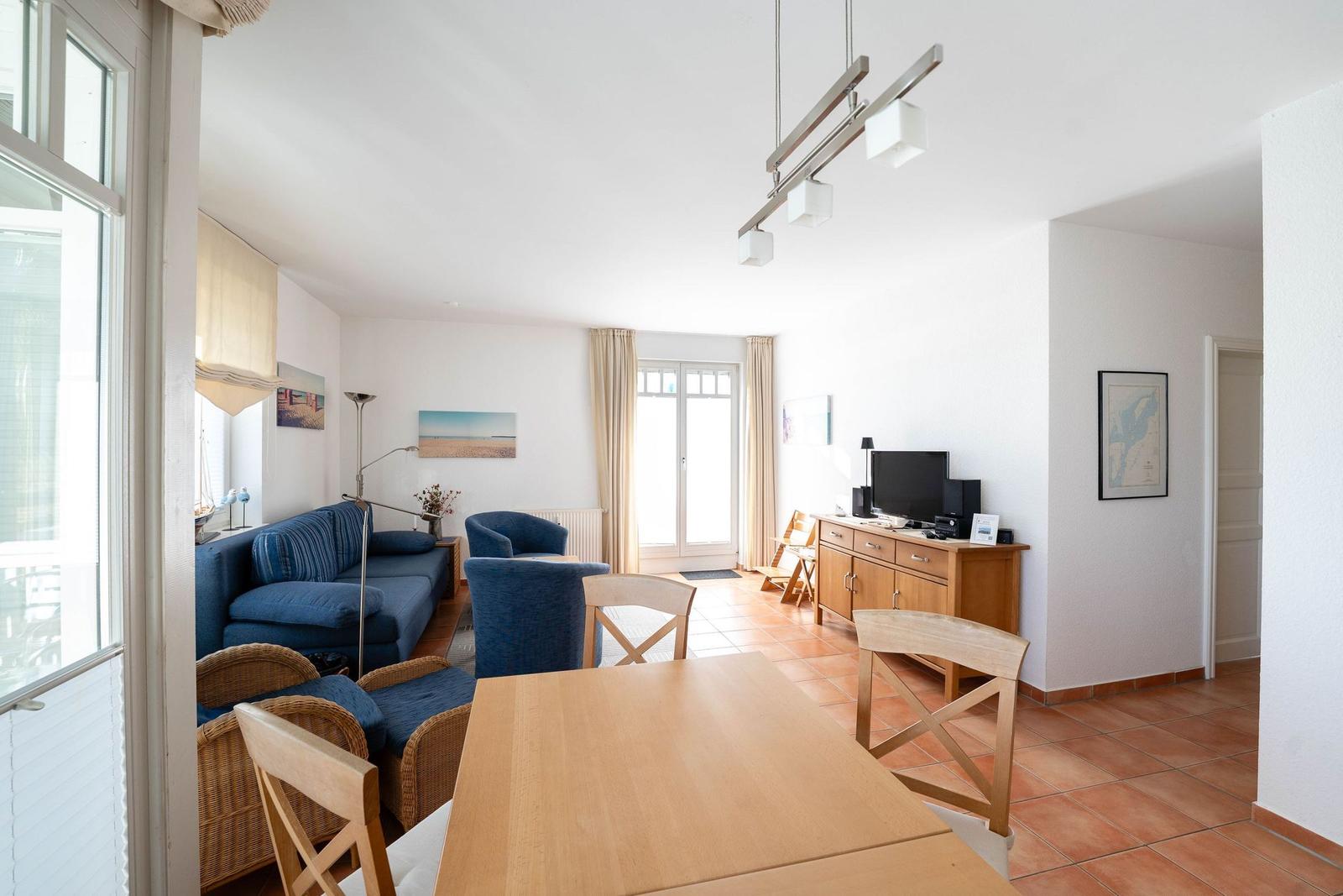 Wohn- und Essbereich mit blauer Couch, Holztisch und Terrassentür.