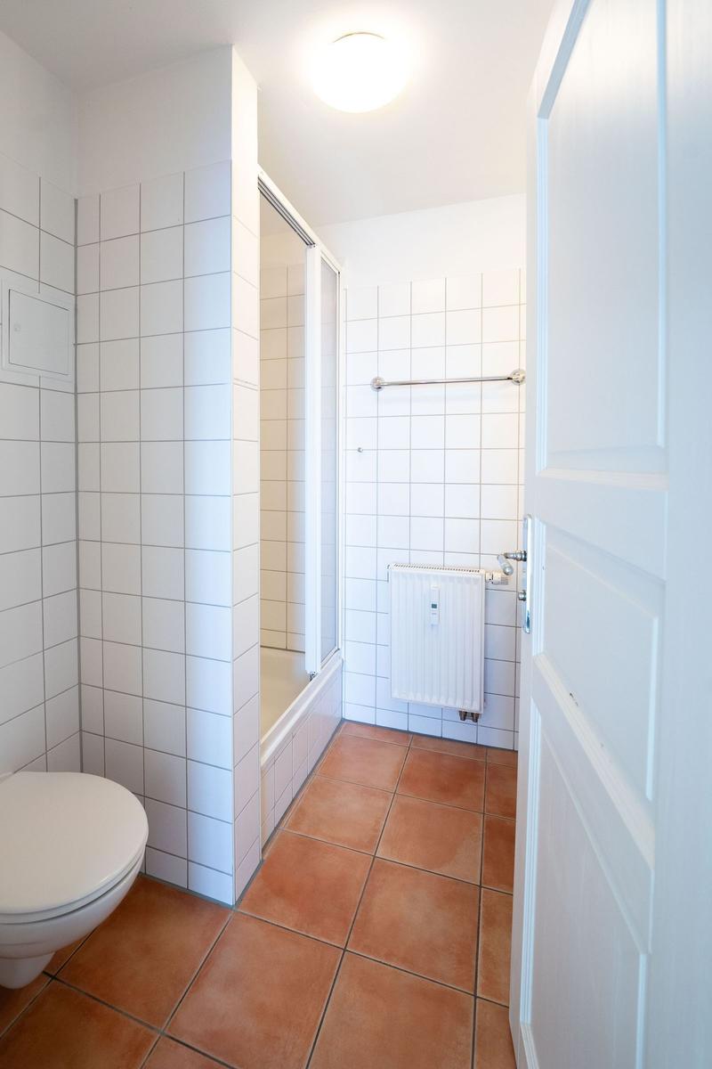 Badezimmer mit Toilette, Dusche und Heizkörper an der Wand.