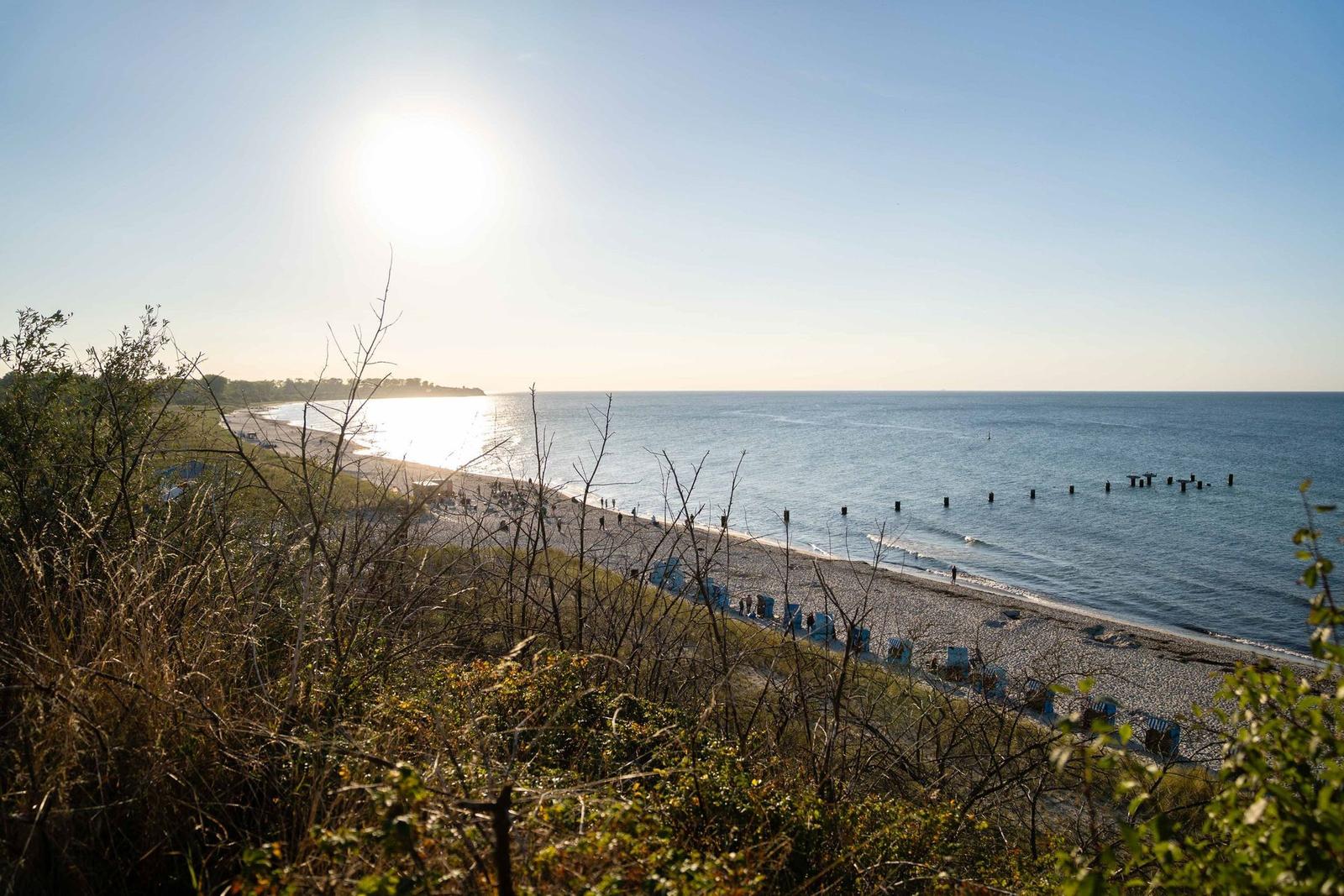 Strand mit Steinen, blauen Strandkörben und Sonne am Horizont.