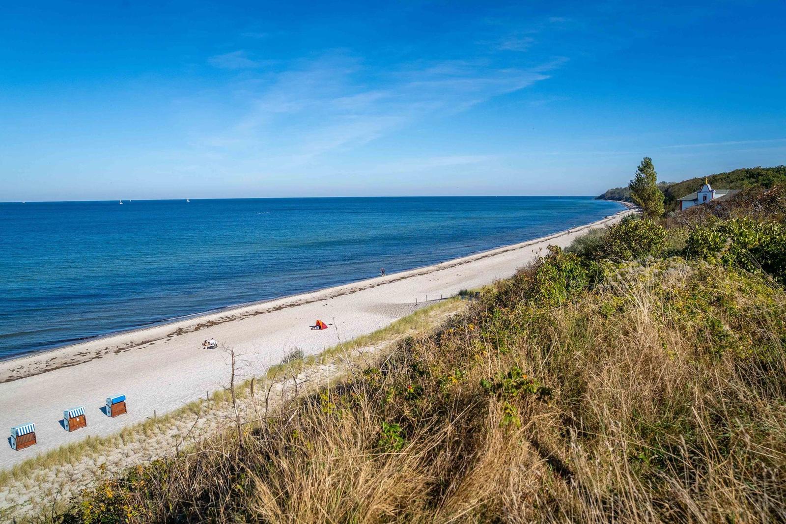 Strand mit Sanddünen, Strandkörben und blauem Meer unter klarem Himmel.