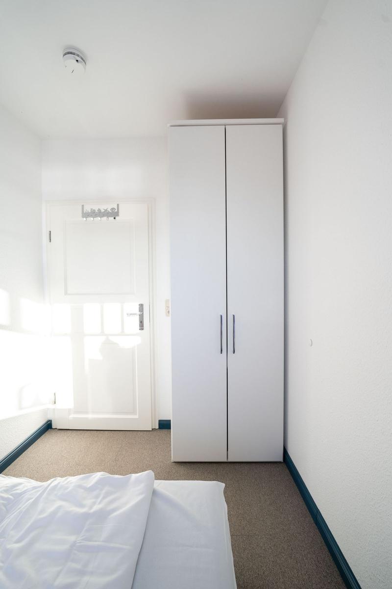 Schlafzimmer mit weißem Kleiderschrank und Bett. Tür mit Haken.