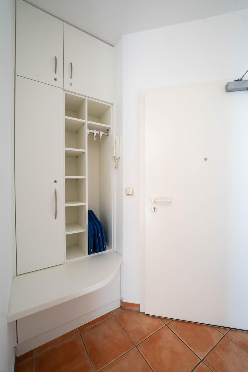 Eingangsbereich mit weißem Schrank und Tür. Blaue Tasche im Schrank.