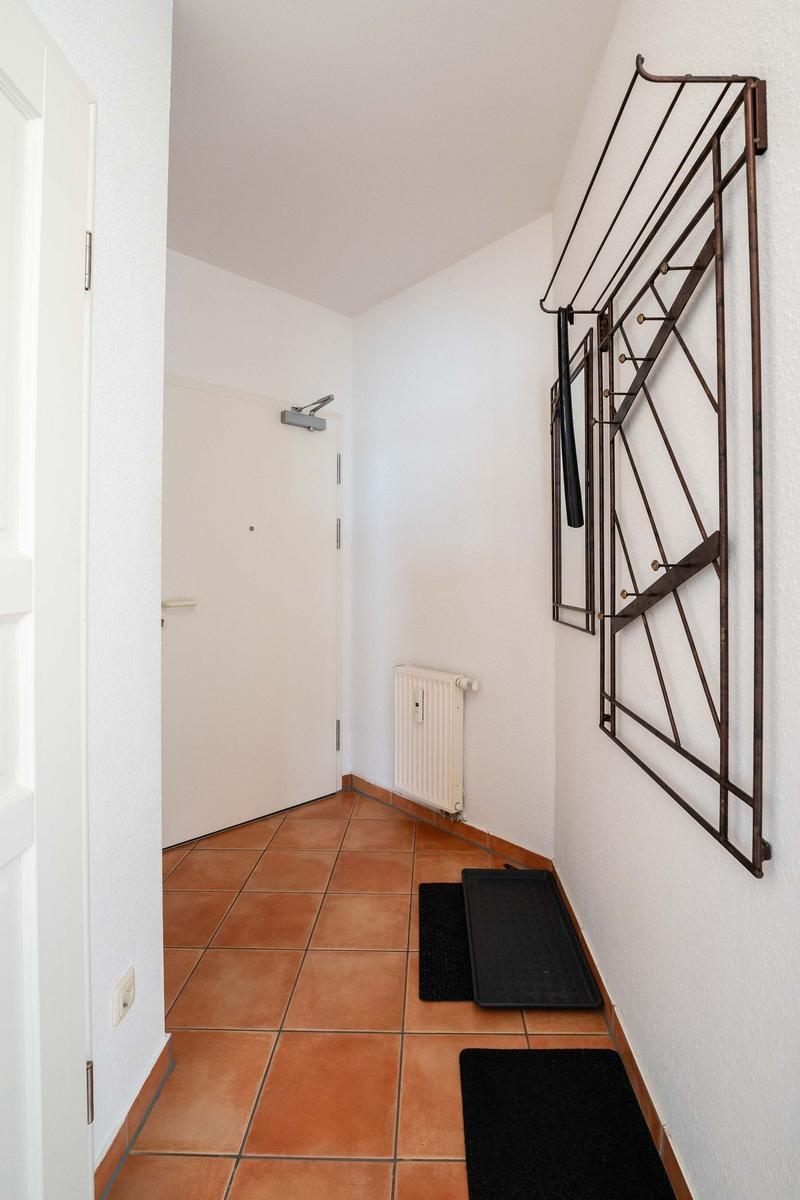 Flur mit Terrakottboden, Heizkörper und Wandgarderobe.
