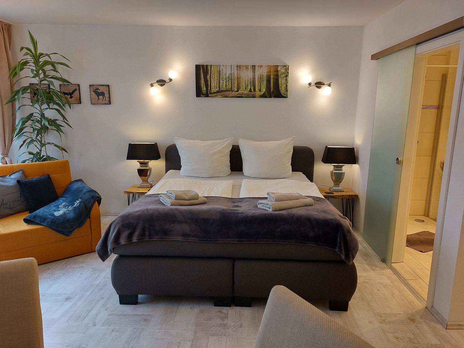 Schlafzimmer mit Bett, Nachttischen und Wandbild. Anschlussbad sichtbar.