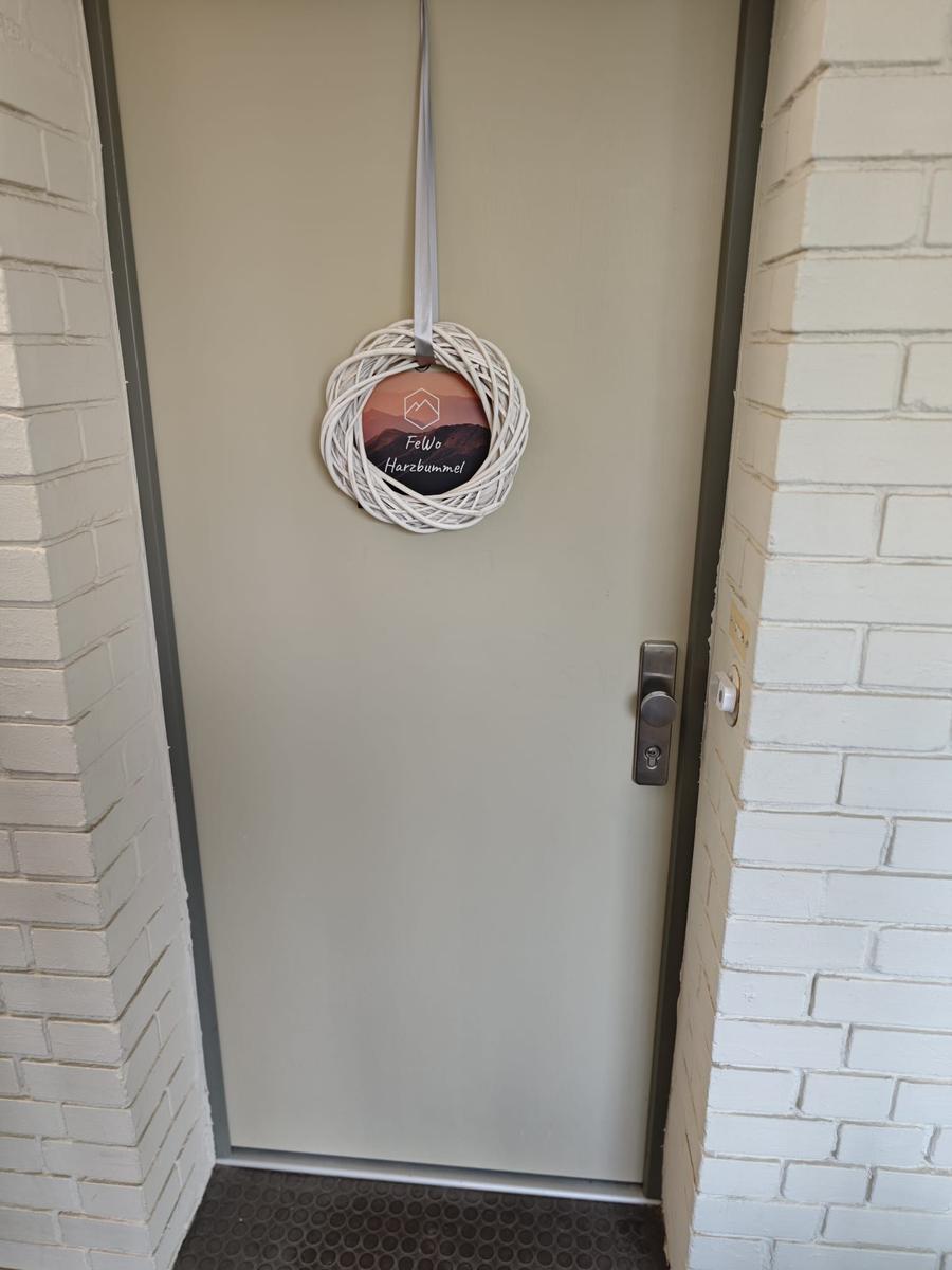 Eingangstür mit Dekorationskranz und Metallgriff zwischen weißen Ziegelwänden.