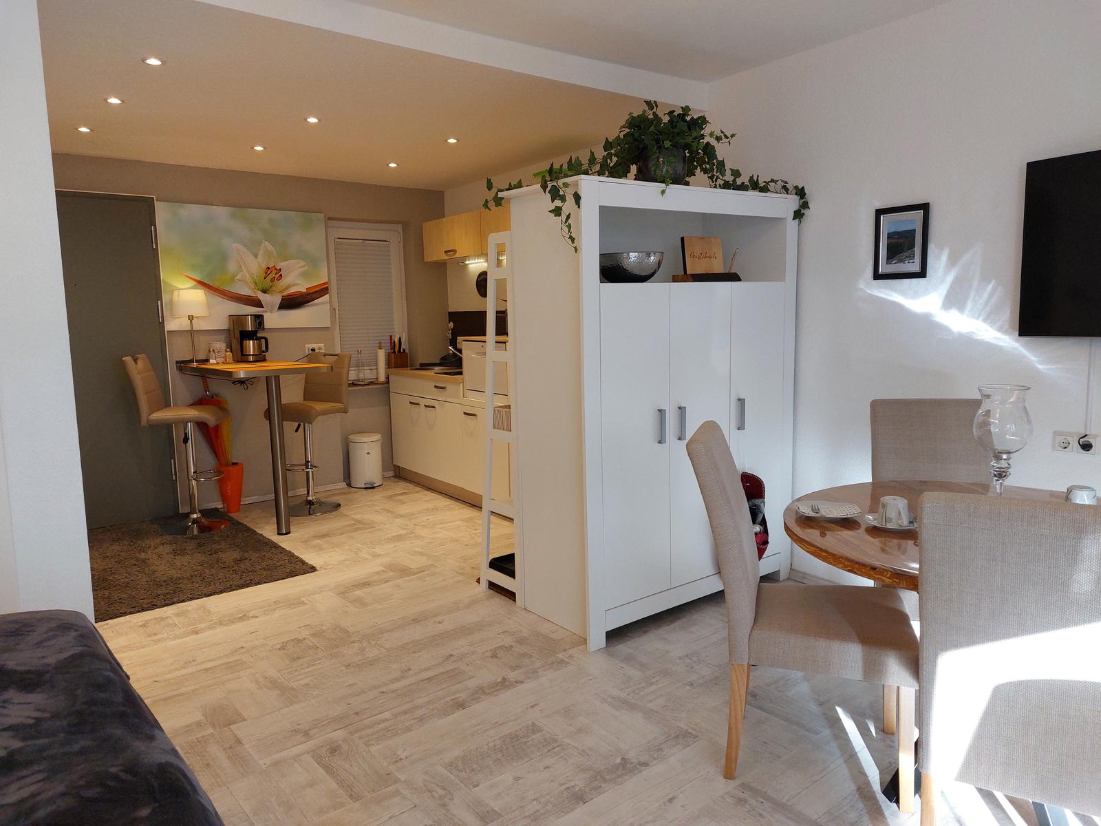 Wohn- und Küchenbereich mit Esstisch, Hochschrank und Barhocker.