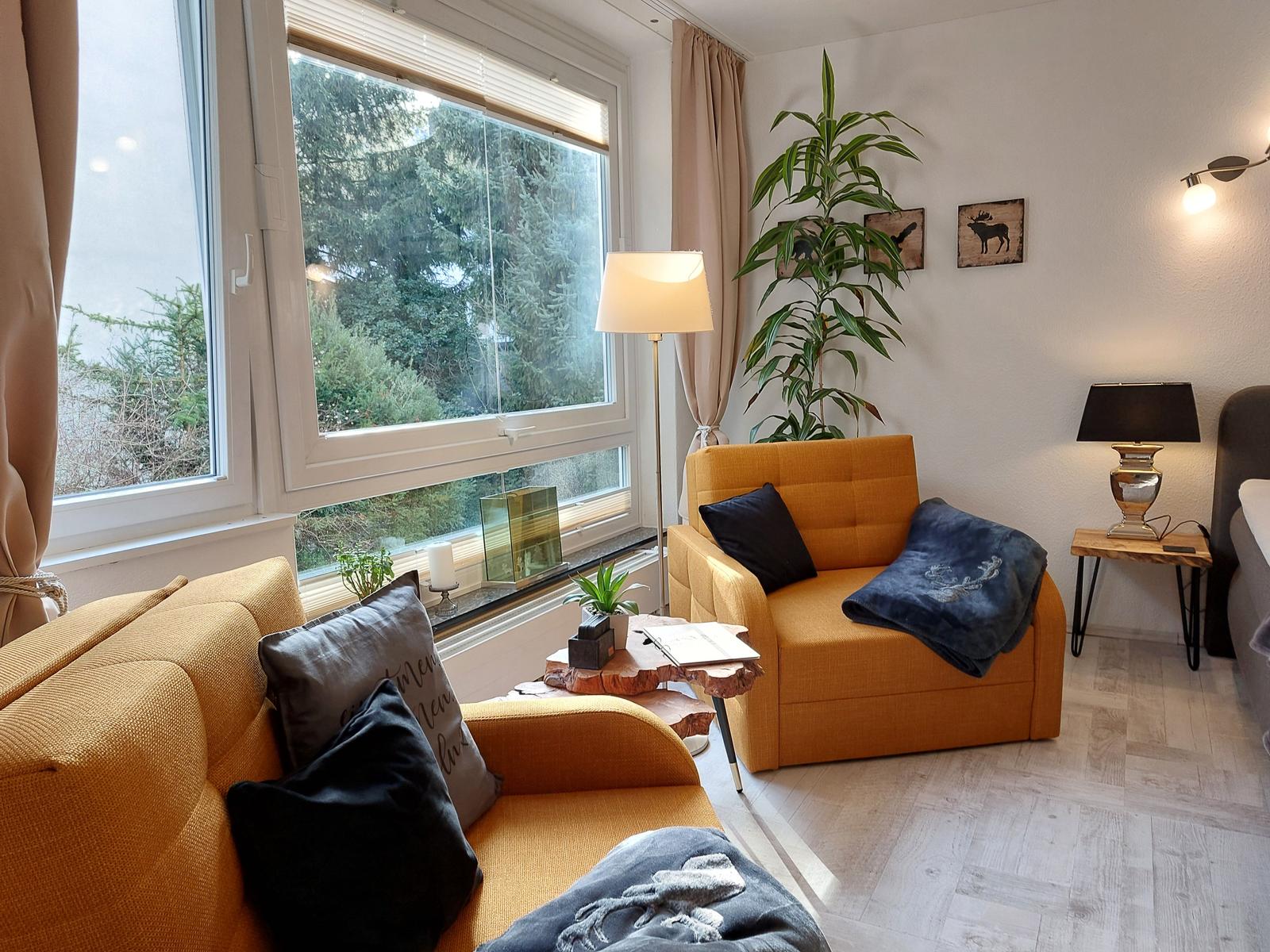 Wohnzimmer mit gelben Sitzmöbeln, großen Fenstern und Zimmerpflanzen.