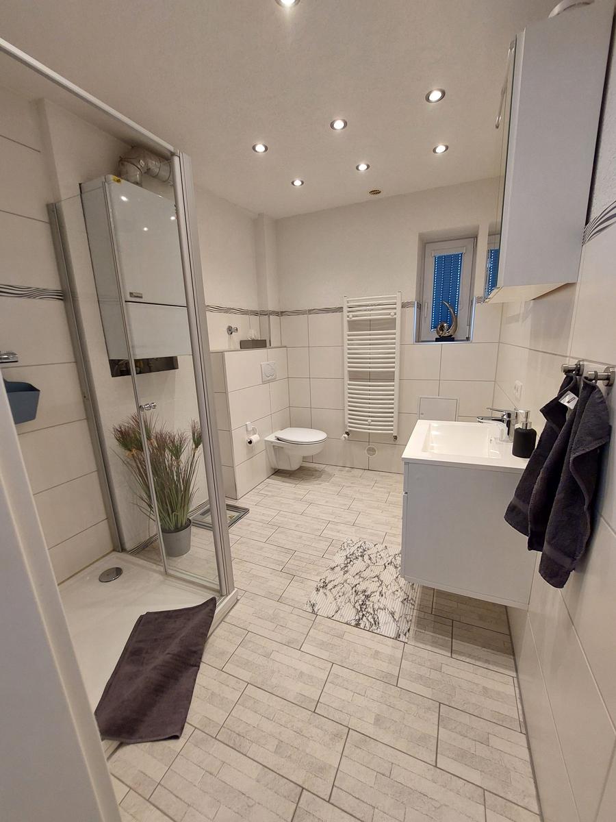 Badezimmer mit Dusche, WC und Waschbecken. Weiße Fliesen und moderne Einrichtung.