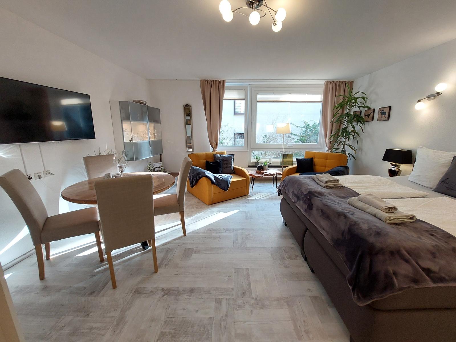 Ein Raum mit Schlaf- und Essbereich, zwei Sesseln und einem großen Fenster.