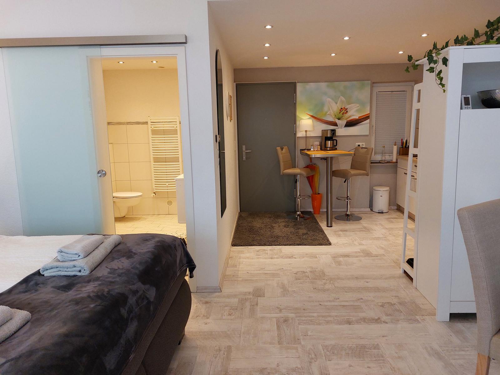 Schlafzimmer mit Blick auf Wohnbereich und Bad. Helle Holzböden und moderne Einrichtung.