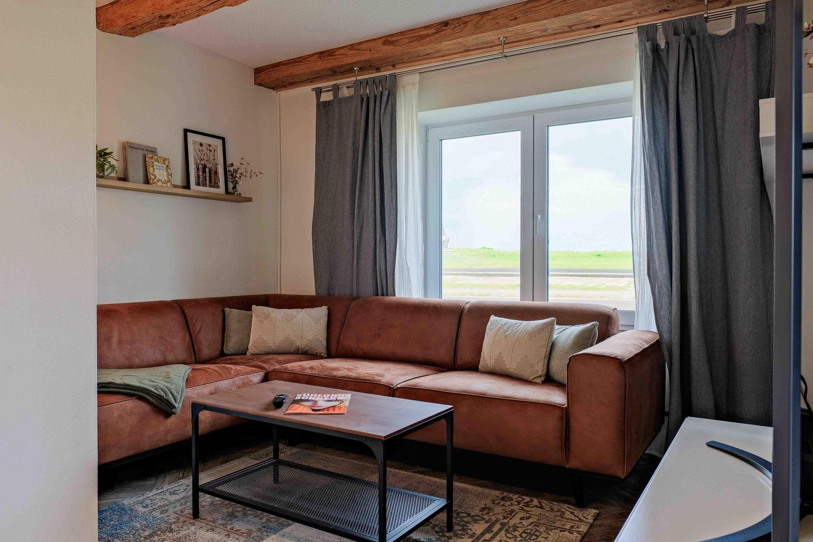 Wohnzimmer mit braunem Sofa, Tisch und Fenster mit Blick auf Grünfläche.