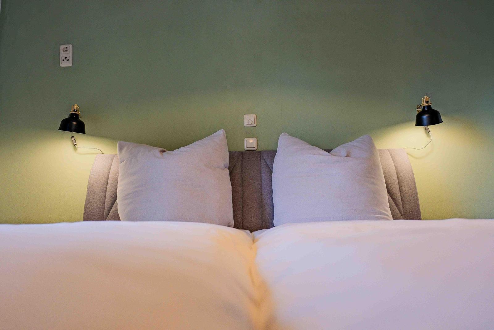 Doppelbett mit Kissen und Wandlampen an grünem Wand