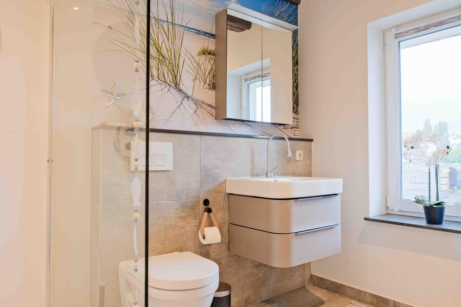 Badezimmer mit Dusche, Waschbecken und Fenster mit Pflanze.