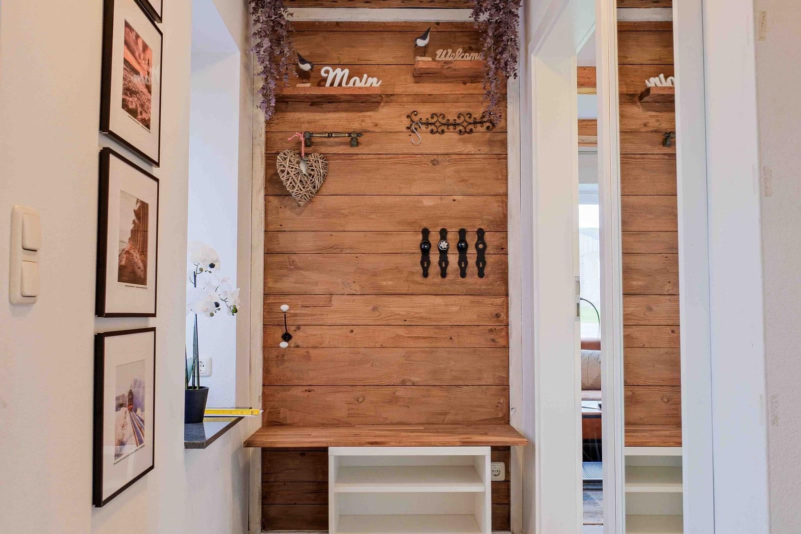Eingangsbereich mit Holzwand, Haken und Sitzbank. Dekoration mit Herz und Blumen.