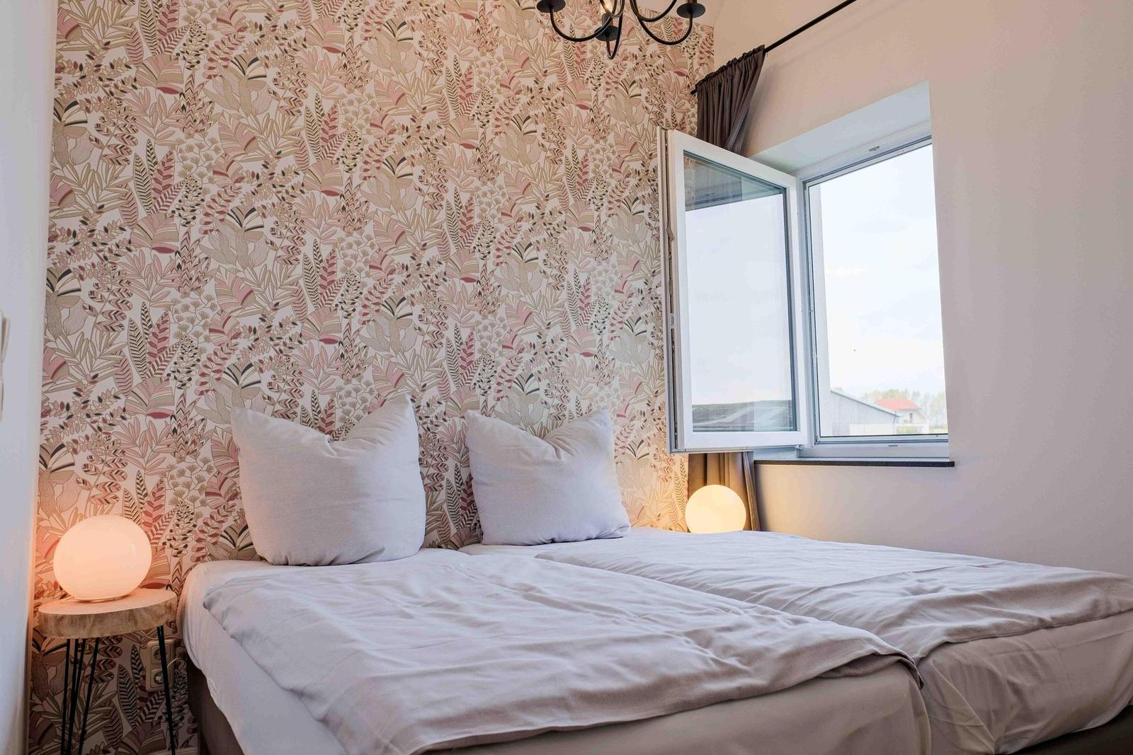 Schlafzimmer mit Bett, Fenster und floraler Tapete.