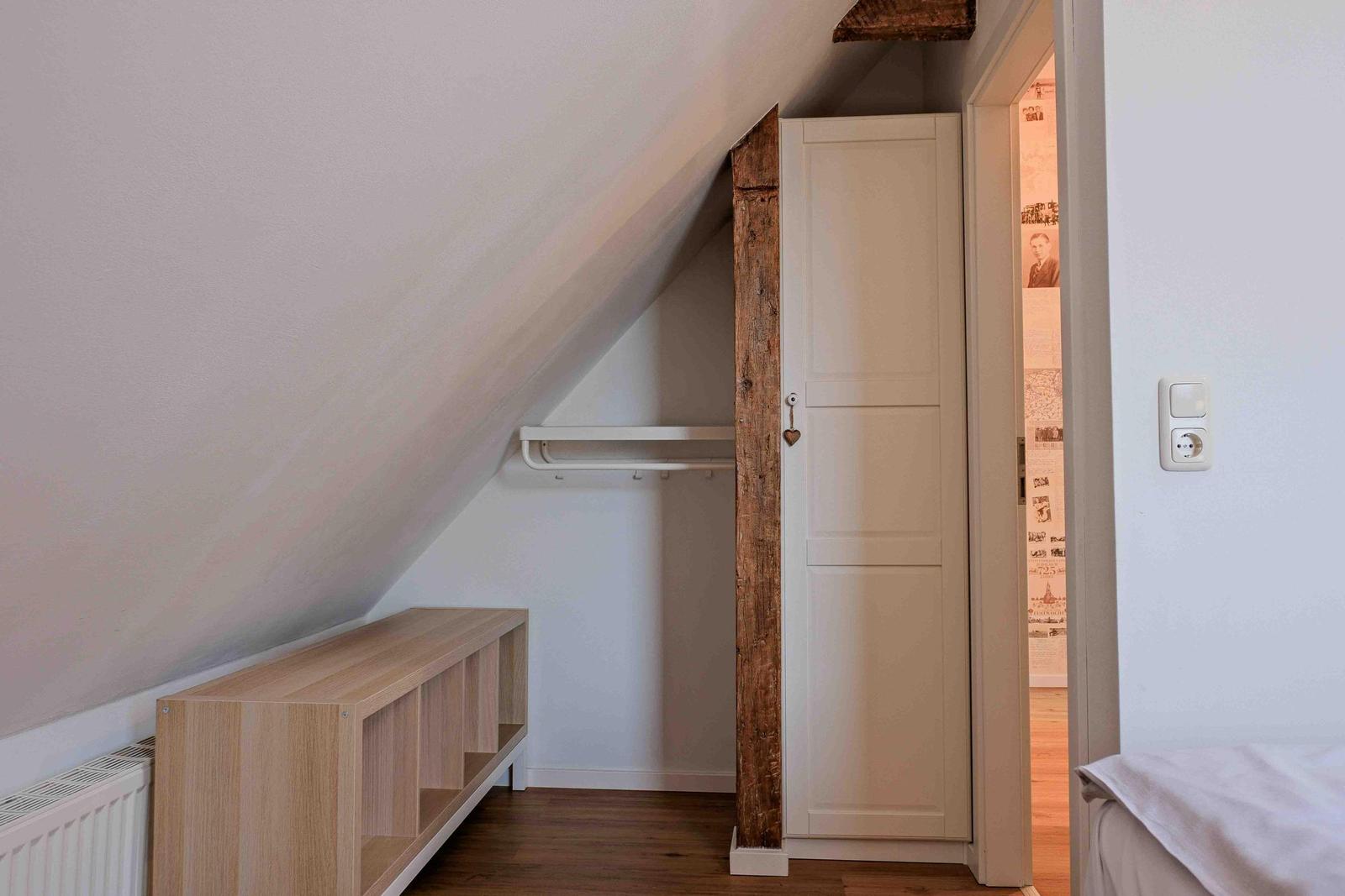 Schlafzimmer mit Dachschrägen, Kleiderschrank und Holzregal.
