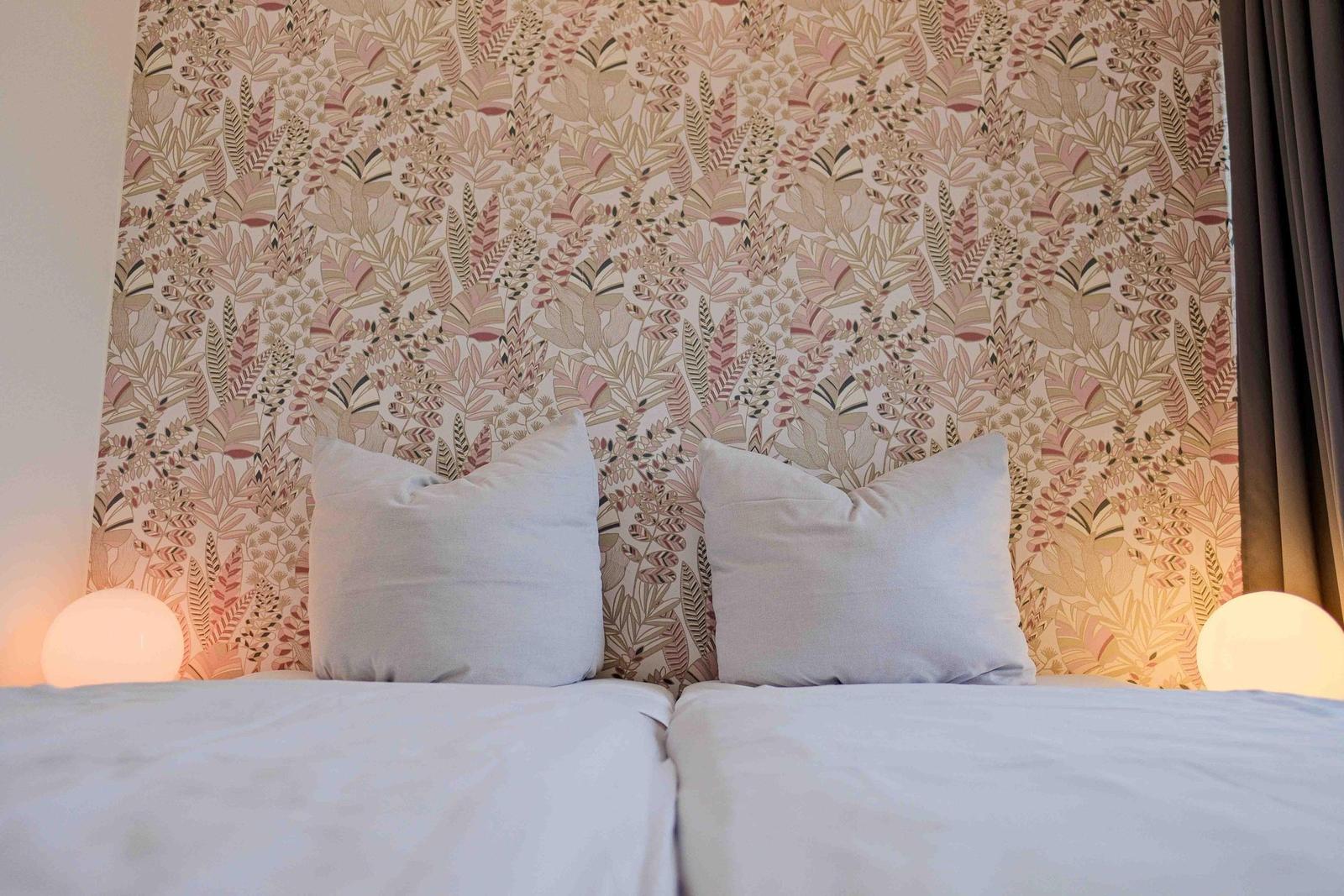 Ein Bett mit weißen Kissen und floraler Tapete im Hintergrund.