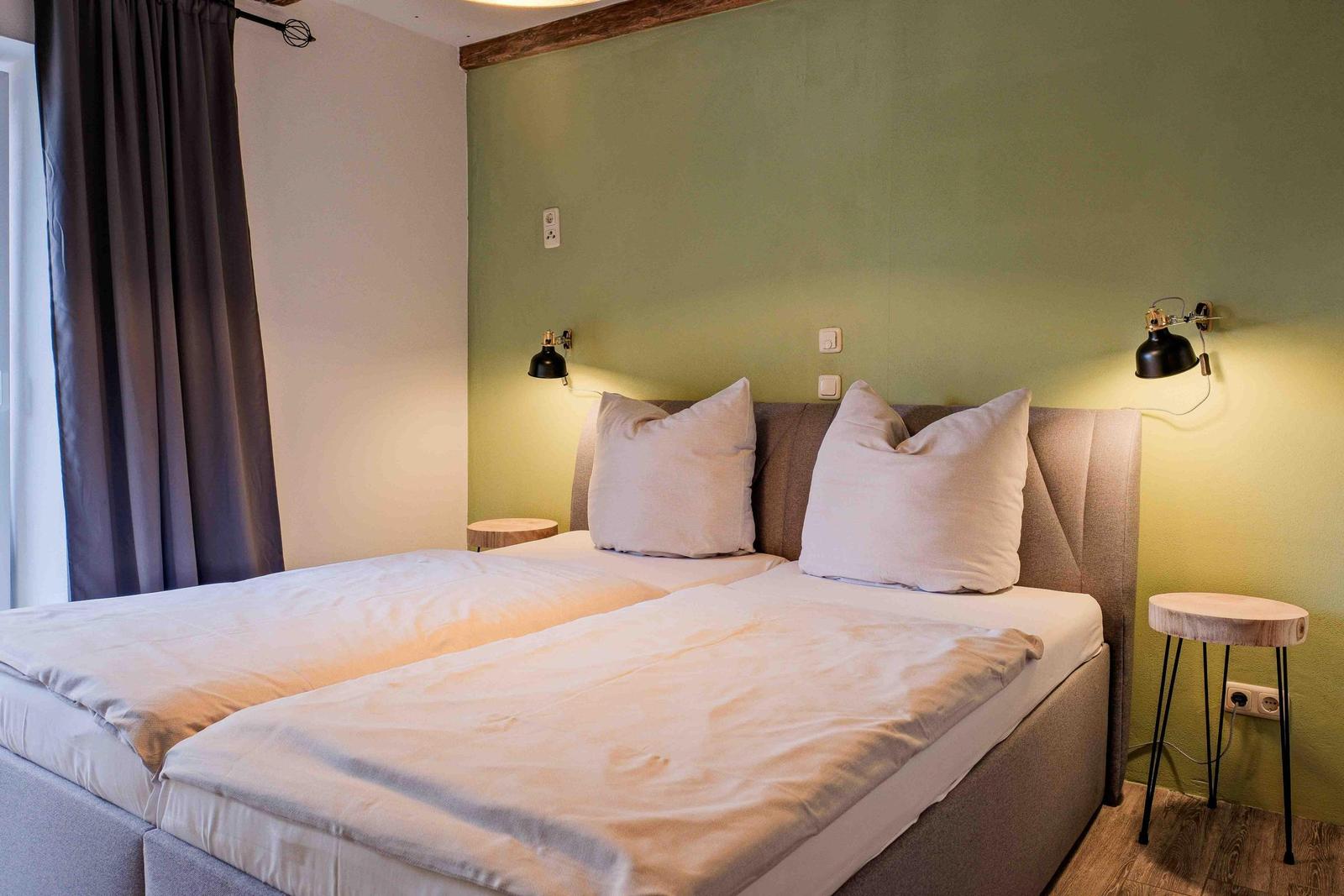 Schlafzimmer mit Doppelbett, grüner Wand und zwei Wandlampen.