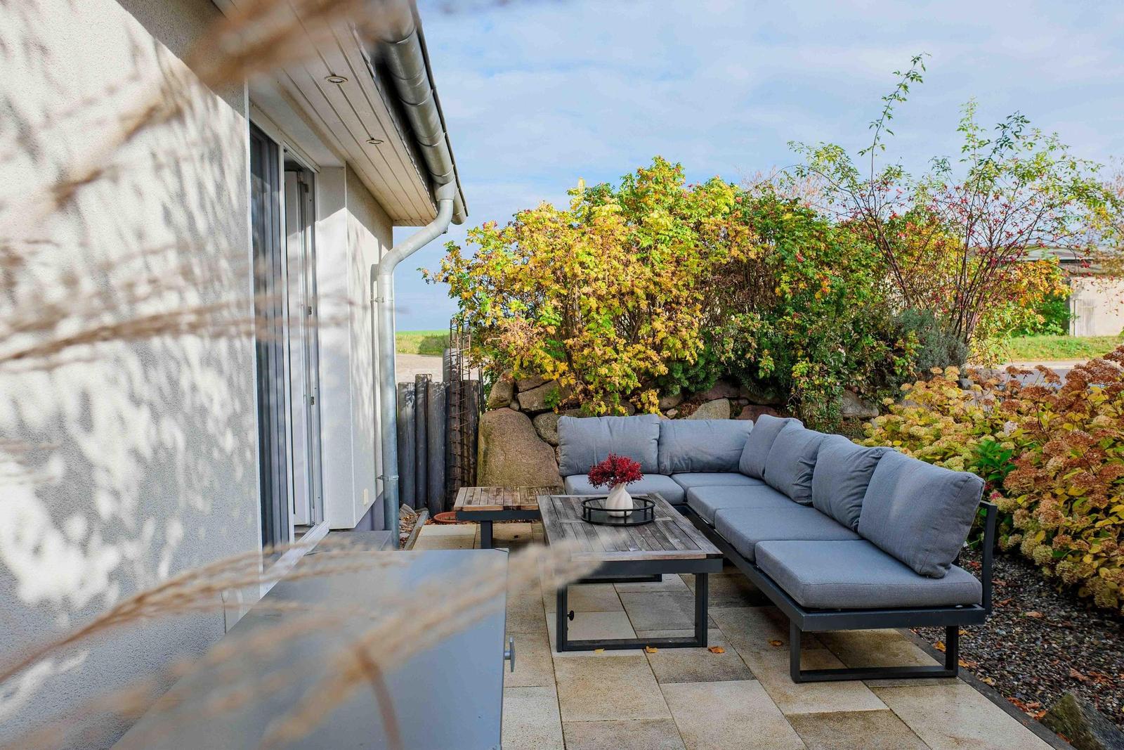 Terrasse mit Sitzgruppe, Tisch und Pflanzen im Herbst.