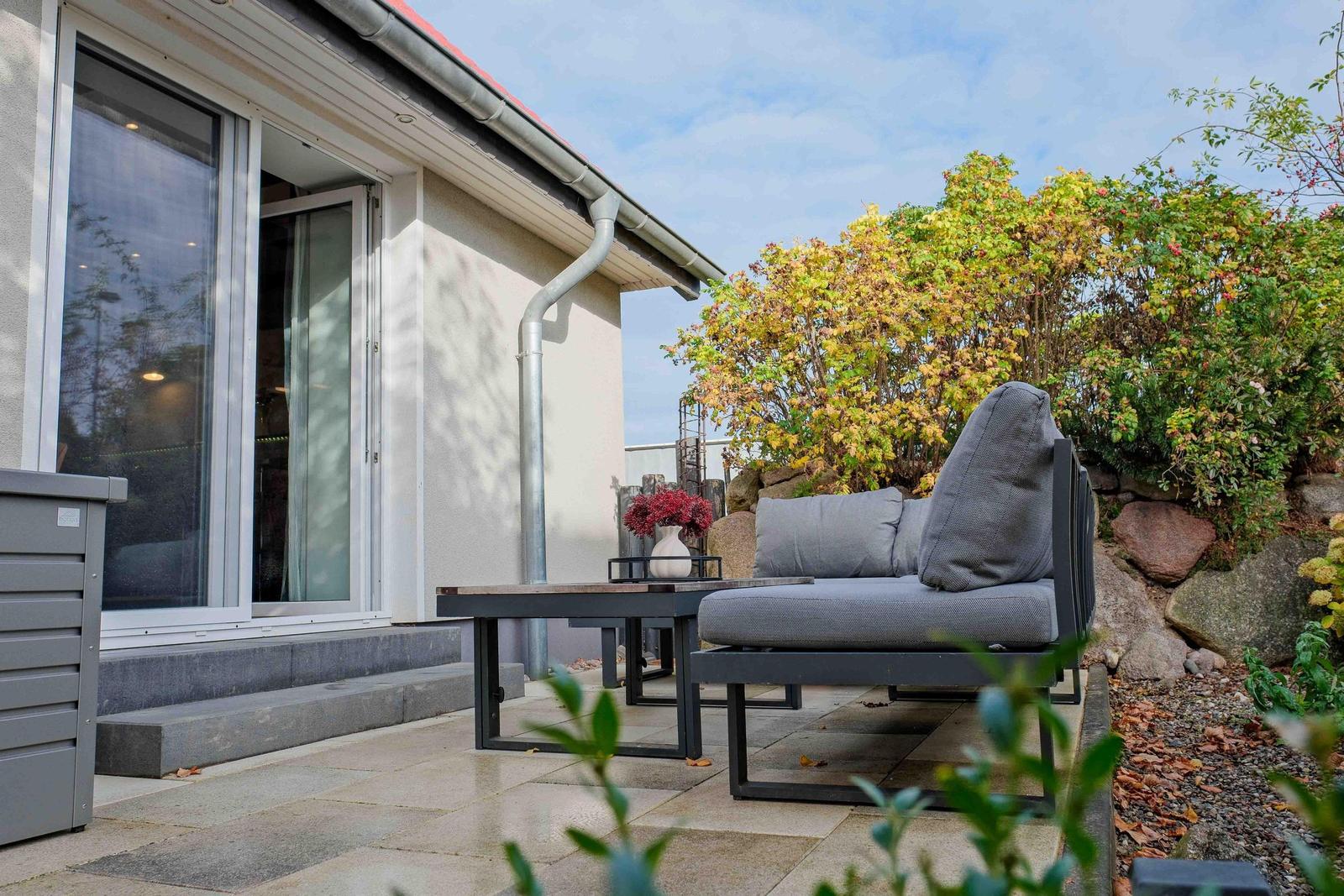 Terrasse mit Sitzgruppe, Tisch und Pflanzen vor Hauswand.