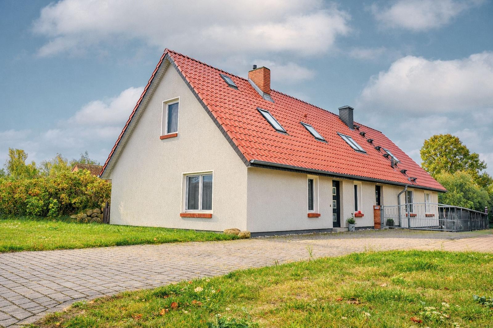 Ein Haus mit rotem Dach und weißen Wänden. Vor dem Haus liegt ein gepflasterter Weg.