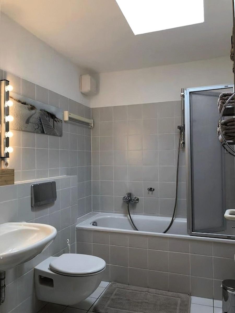 Badezimmer mit Badewanne, Dusche, Waschbecken und Toilette. Dachfenster sorgt für Tageslicht.