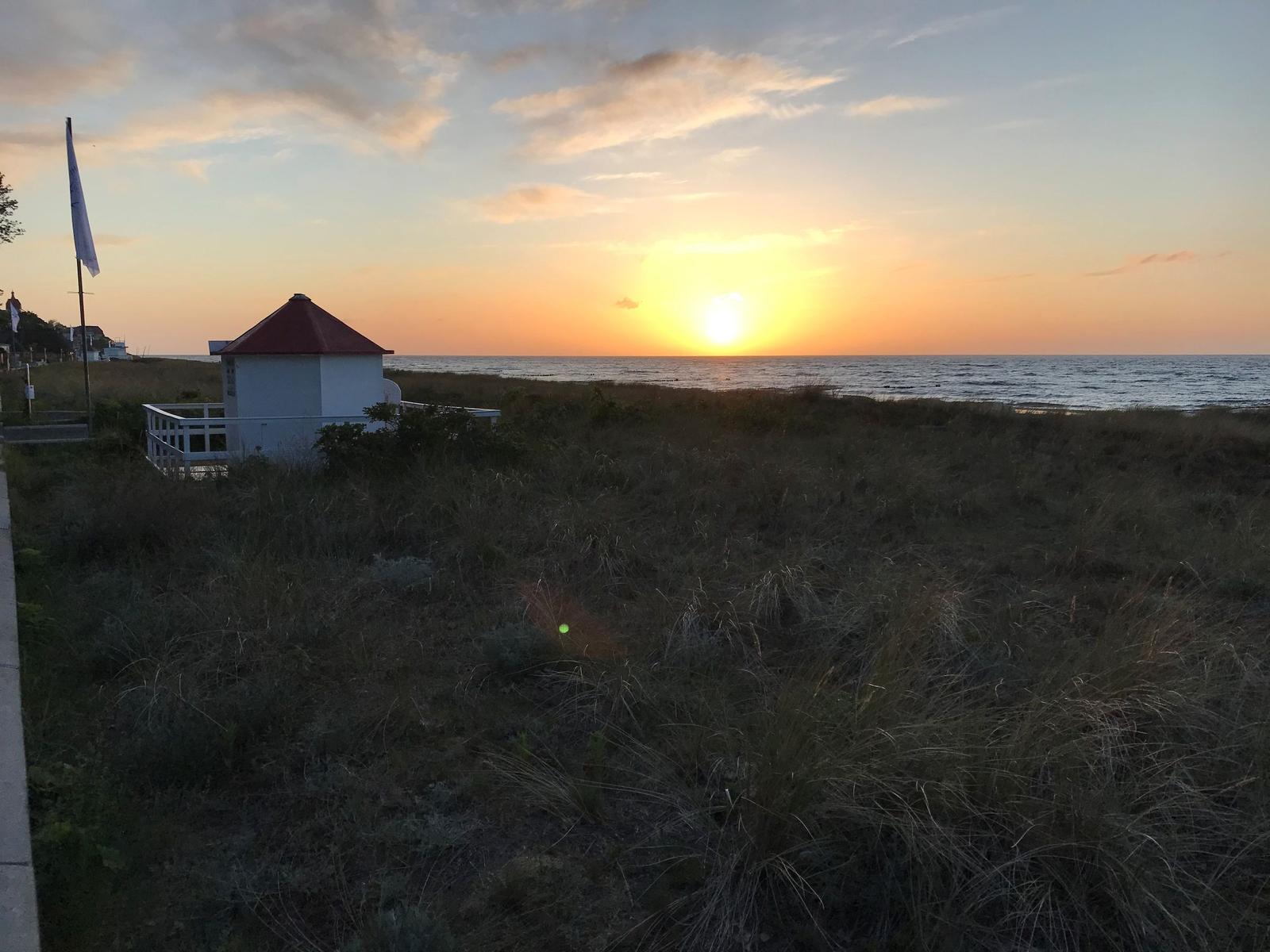 Sonnenuntergang am Strand mit kleinem weißen Gebäude und rotem Dach.