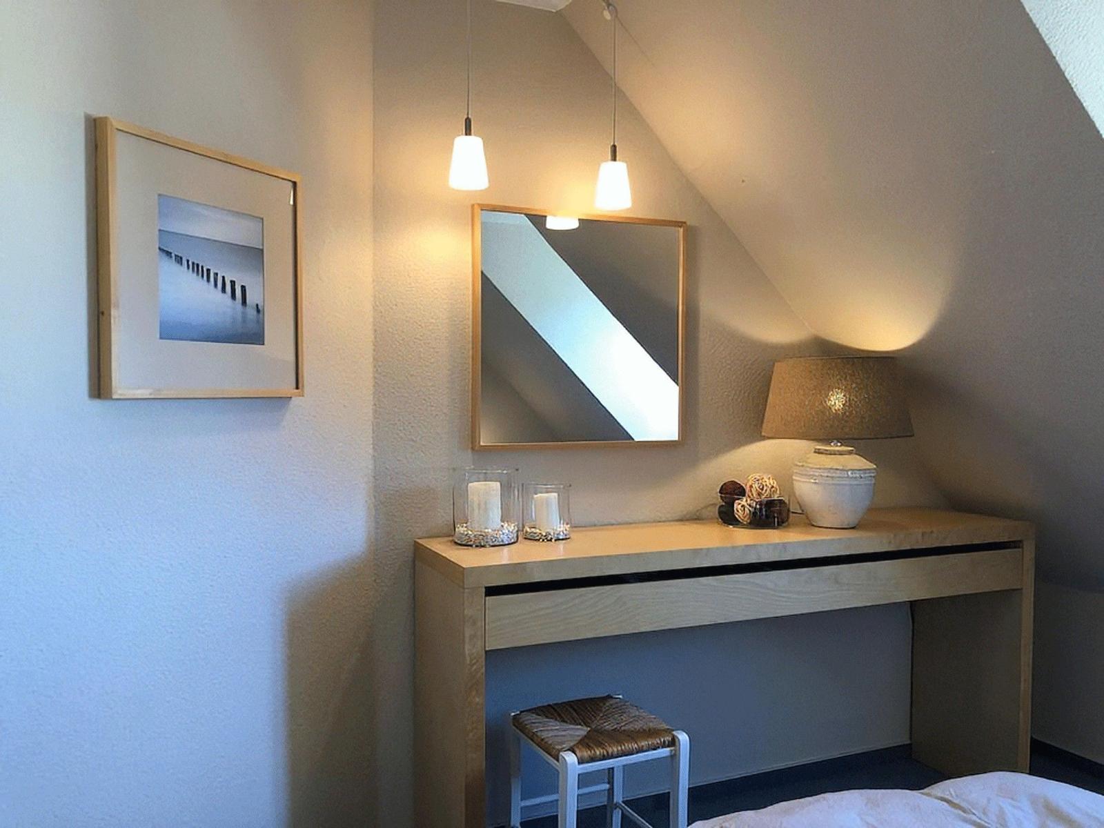Schreibtisch mit Spiegel, Lampe und Bild an der Wand unter Dachschräge.