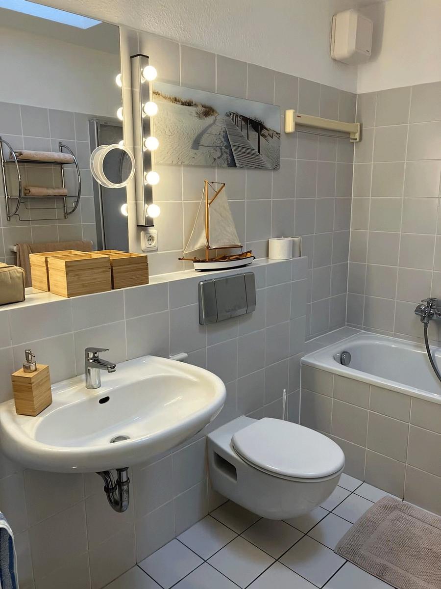 Badezimmer mit Badewanne, Waschbecken und Toilette. Wandbild und Segelschiffmodell.