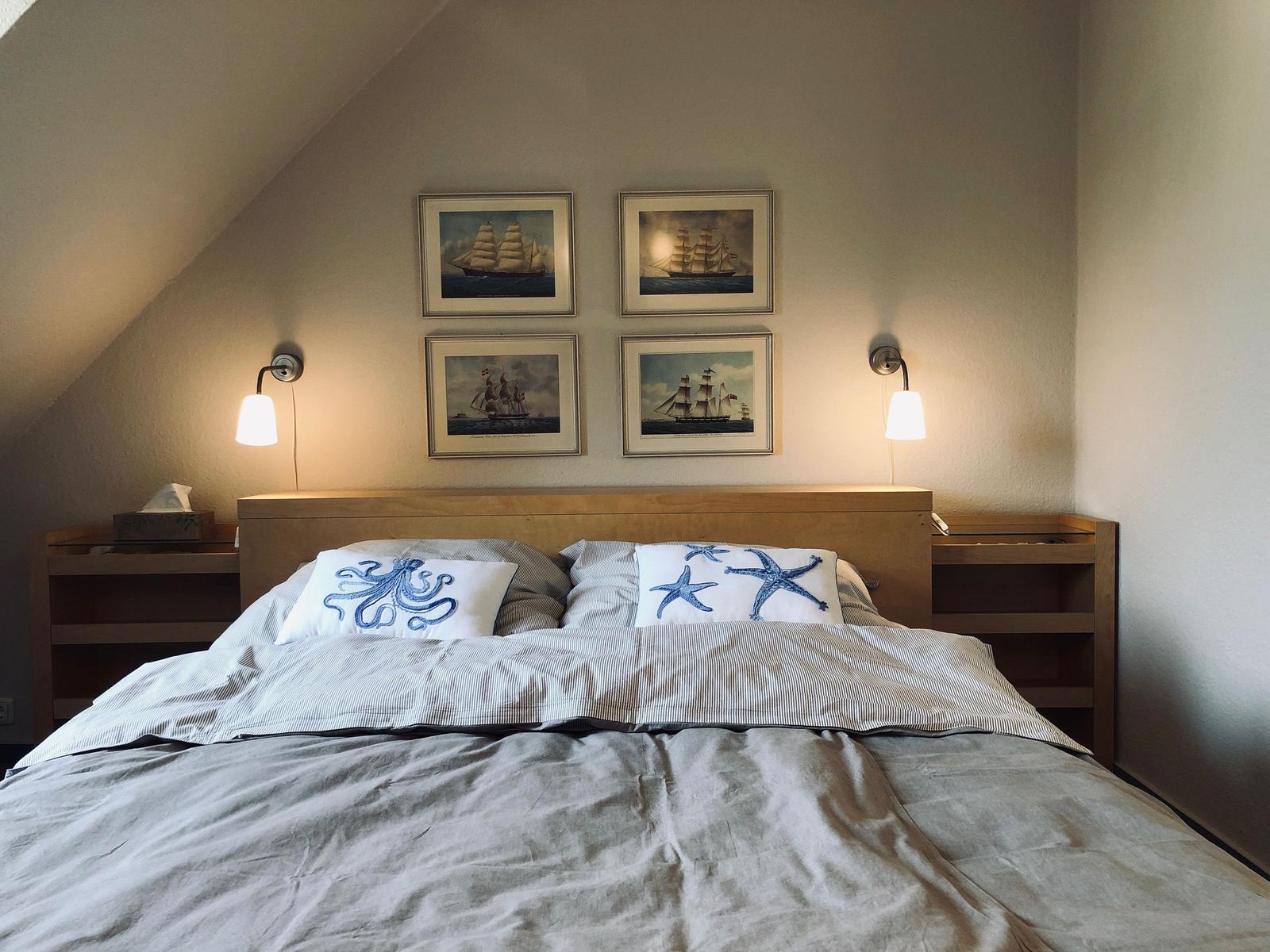 Schlafzimmer mit Bett, Wandbildern und Nachttischen unter Dachschrägen.
